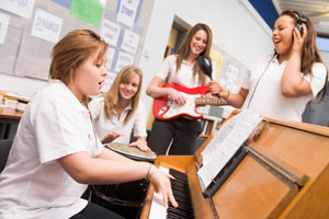 Four high school girls rehersing in the music room on piano, drums, guitar and singing.