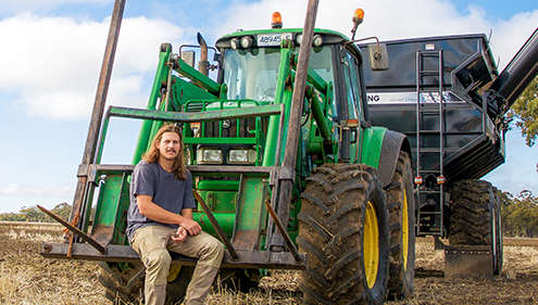 A male VET Agriculture student sitting in front of harvester machine